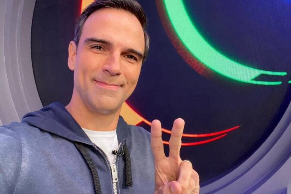 Tadeu Schmidt é homem branco que usa cabelo curto preto liso, camisa branca e blusa de frio cinza na imagem